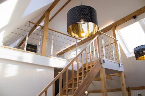 Blick hinauf zur Schlafgalerie in der Ferienwohnung Fronhof, geprägt von Holzbalken, einer Holztreppe und großen Deckenleuchten