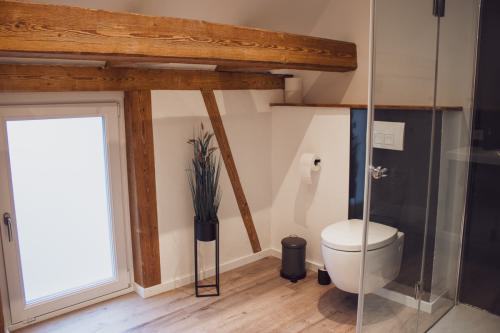 Badezimmer mit einem großen bodentiefen Fenster, das viel Tageslicht hereinlässt, und charakteristischen Holzbalken an der Decke.